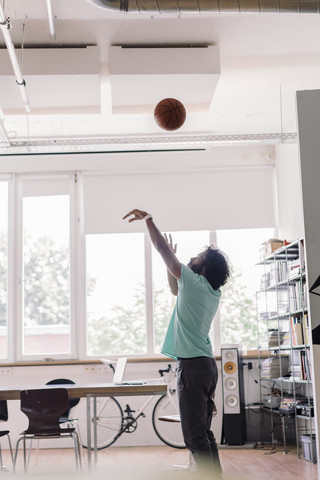 Junger Mann spielt mit Basketball im Büro, lizenzfreies Stockfoto