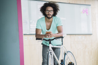 Young man leaning on bicycle, using smart phone - RIBF000552