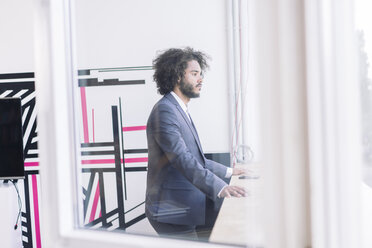 Young businessman standing by window, thinking - RIBF000565