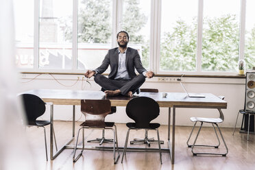 Young businessman sitting cross-legged on desk in office - RIBF000577