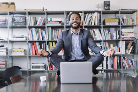 Young businessman sitting in office meditating in front of laptop stock photo