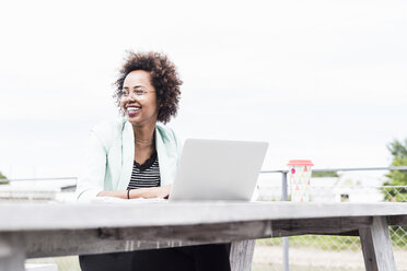 Lächelnde Geschäftsfrau bei der Arbeit mit ihrem Laptop im Freien - UUF008172