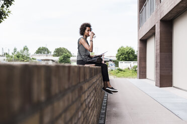 Young woman sitting on wall drinking coffee to go - UUF008195