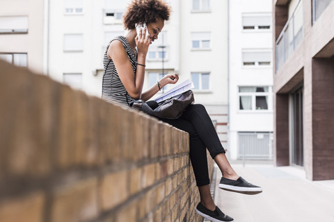 Junge Frau sitzt an der Wand und telefoniert mit einem Handy, lizenzfreies Stockfoto