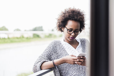 Woman standing on balcony looking at cell phone - UUF008206