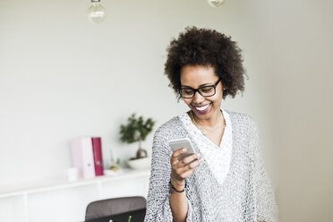 Lächelnde Geschäftsfrau im Büro, die auf ihr Smartphone schaut - UUF008210