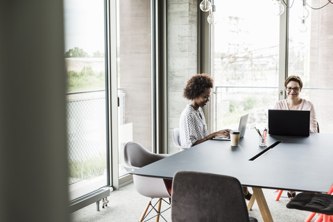 Two smiling women working at laptops in an office stock photo