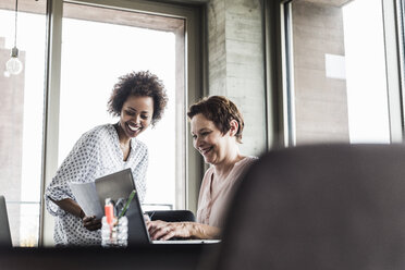 Zwei lächelnde Frauen arbeiten zusammen in einem Büro - UUF008218