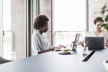 Zwei Geschäftsfrauen sitzen am Schreibtisch und arbeiten mit einem Laptop - UUF008224