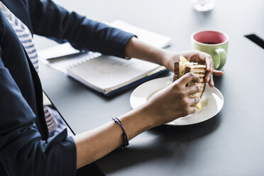 Geschäftsfrau sitzt am Schreibtisch und nimmt ein Sandwich ein, Teilansicht - UUF008252