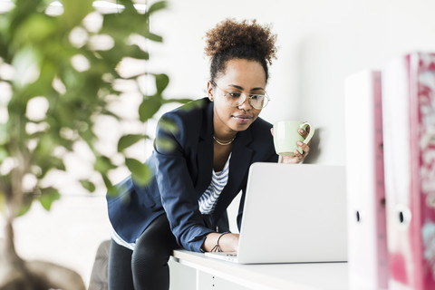 Businesswoman with cup of coffee looking at laptop stock photo