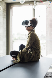 Frau im Büro sitzt am Konferenztisch und trägt eine Virtual-Reality-Brille - UUF008261