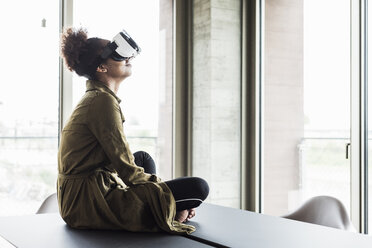 Frau im Büro sitzt am Konferenztisch und trägt eine Virtual-Reality-Brille - UUF008262