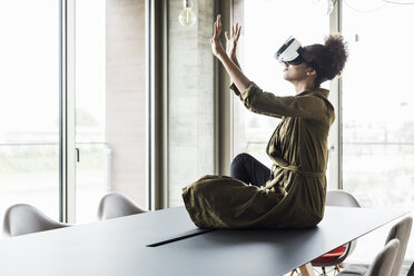 Frau im Büro sitzt am Konferenztisch und benutzt eine Virtual-Reality-Brille - UUF008263