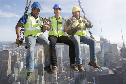 Three construction workers sitting on suspended scaffolding high above city having lunch - ZEF009161