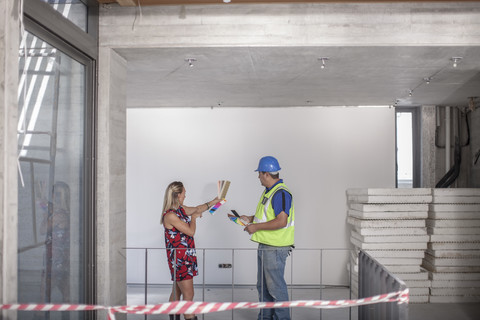 Bauarbeiter und Frau mit Farbmuster auf einer Baustelle, lizenzfreies Stockfoto