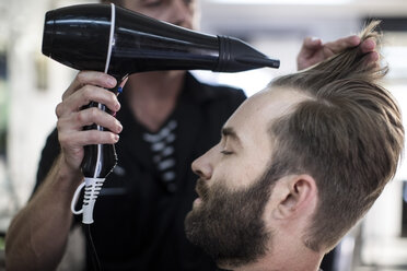 Friseur föhnt das Haar eines Kunden - ZEF009205
