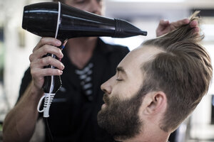 Friseur föhnt das Haar eines Kunden - ZEF009205