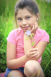 Porträt eines lächelnden Mädchens mit Blume auf einer Wiese sitzend - VTF000540