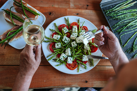 Senior man eating salad of green asparagus, tomatoes and sheep cheese accompanied by white wine stock photo