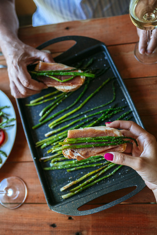 Hände nehmen Brotscheiben mit Schinken und gegrilltem grünen Spargel, lizenzfreies Stockfoto