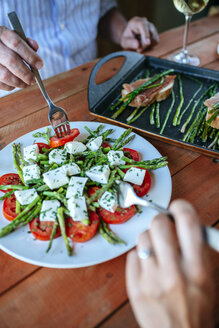 Hände von zwei Personen, die einen Salat mit grünem Spargel, Tomatenscheiben und Schafskäsewürfeln essen - KIJF000614