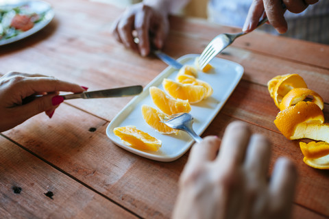 Hände von zwei Personen, die Orangenscheiben mit Besteck essen, lizenzfreies Stockfoto