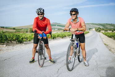 Spanien, Andalusien, Jerez de la Frontera, Paar, Radfahrer auf einer Landstraße zwischen Weinbergen - KIJF000622