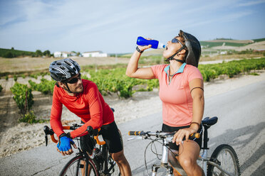 Spanien, Andalusien, Jerez de la Frontera, Radfahrerpaar trinkt Wasser auf einer Landstraße zwischen Weinbergen - KIJF000623