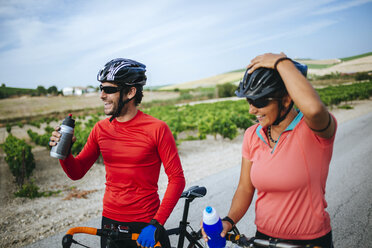 Spanien, Andalusien, Jerez de la Frontera, Radfahrerpaar trinkt Wasser auf einer Landstraße zwischen Weinbergen - KIJF000624