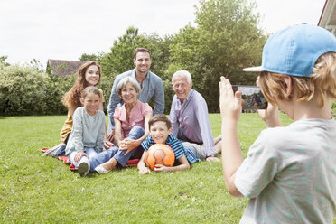Boy taking picture of happy extended family in garden - RBF004760