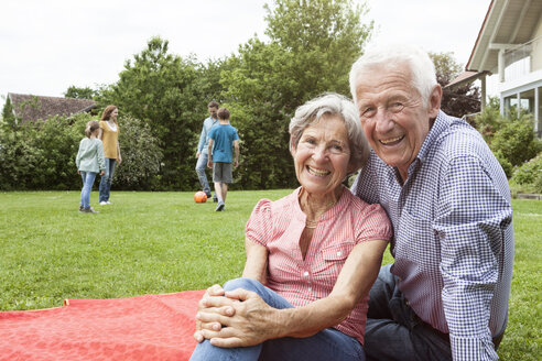 Porträt eines glücklichen älteren Paares mit Familie im Hintergrund im Garten - RBF004762