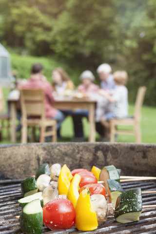 Gemüsespieße auf dem Grill mit Familie im Hintergrund, lizenzfreies Stockfoto