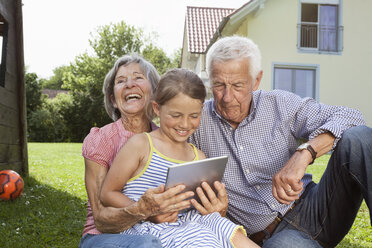 Grandparents and granddaughter in garden using digital tablet - RBF004800