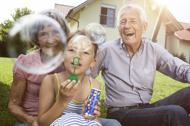 Großeltern und Enkelin im Garten beim Blasen von Seifenblasen - RBF004802