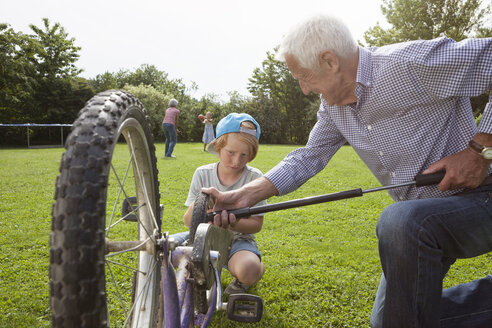 Großvater bläst das Fahrrad des Enkels im Garten auf - RBF004806
