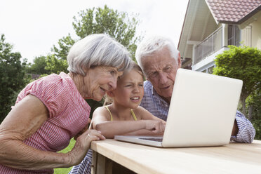 Großeltern und Enkelin benutzen Laptop im Garten - RBF004808