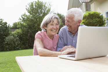 Glückliches älteres Paar benutzt Laptop im Garten - RBF004810