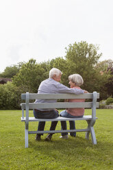 Glückliches älteres Paar sitzt auf einer Bank im Garten - RBF004816