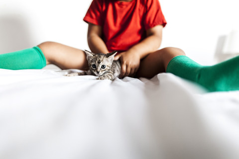 Kleiner Junge sitzt auf dem Bett und hält ein Kätzchen, lizenzfreies Stockfoto