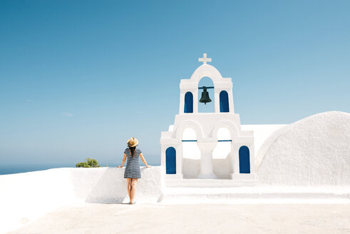 Greece, Santorini, Oia, back view of woman standing next to bell tower looking to the sea - GEMF000930