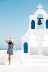 Greece, Santorini, Oia, back view of woman standing next to bell tower looking to the sea - GEMF000932