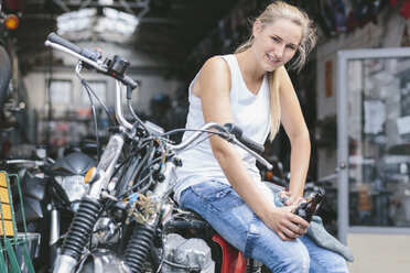 Lächelnde junge Frau mit Bierflasche auf Motorrad - MADF001043