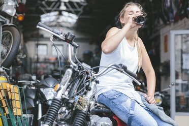 Junge Frau trinkt Bier aus einer Flasche auf einem Motorrad - MADF001044