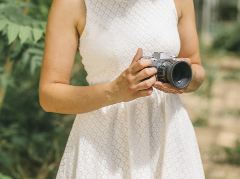 Junge Frau im weißen Kleid hält Kamera, lizenzfreies Stockfoto