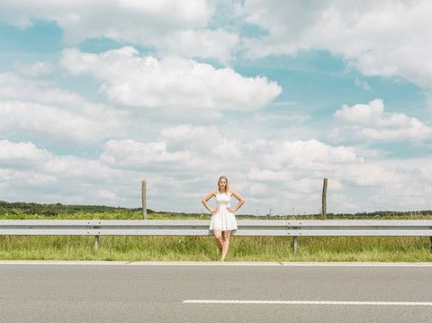 Junge Frau in weißem Kleid steht am Straßenrand, lizenzfreies Stockfoto