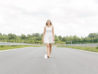 Young woman in white dress walking barefoot on country road - MADF001056