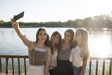 Vier Freunde stehen im Sonnenlicht vor dem Wasser und machen ein Selfie mit ihrem Smartphone - ABZF000879