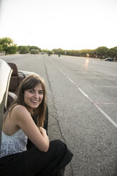 Smiling young woman crouching beside convertible - ABZF000885