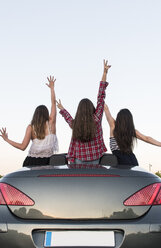 Rückenansicht von drei Freunden, die mit erhobenen Armen in einem Cabrio stehen - ABZF000888